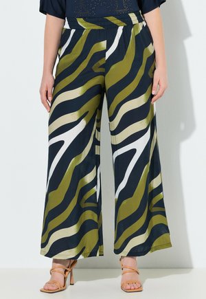 Bukser med vide ben med abstrakt olivengrøn, sort og hvid zebra-lignende mønster, båret med sort top og tanfarvede stropper på højhælede sandaler.