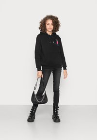 Hoodie preto com bolso frontal e cordões, decorado com bordado colorido. Combinado com jeans skinny pretos e botas robustas com fivela.