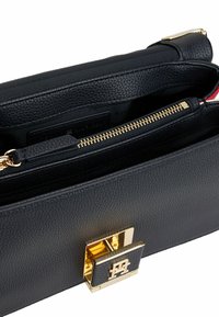 Sac à main en cuir noir texturé avec un fermoir en métal doré. L'intérieur comprend une poche zippée et un revêtement en tissu aux couleurs contrastées.