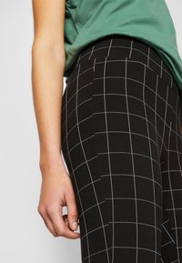 Sorte leggings med et hvitt rutemønster, laget av elastisk stoff, med en glatt tekstur og en tettsittende passform langs benet.