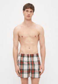 Shorts de bain à carreaux multicolores avec des motifs rouges, verts et bleus, dotés d'une ceinture élastique et de poches latérales. Tissu léger et lisse.