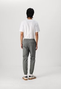 Grå, joggerbyxor med elastisk midja och samlade muddar, i kombination med en enkel vit T-shirt och krämfärgade sneakers med svarta accenter.