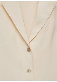Camicia button-up color crema con colletto a punte, texture morbida, due dettagli con bottoni e finitura di tessuto liscia.