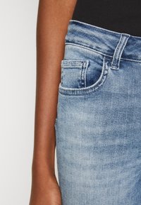 Jeans in denim blu sbiadito con un classico design a cinque tasche, chiusura con bottone e una vita stretta visibile nell'immagine.