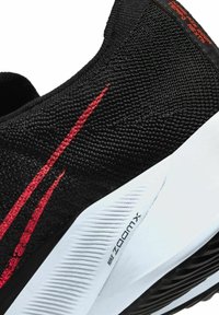 Gros plan sur une chaussure de course Nike ZoomX noire avec un logo swoosh rouge et une semelle intermédiaire blanche texturée.