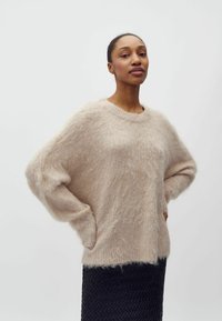 Beige siledav kampsun, millel on ümar kaelus, langenud õlad ja pikad varrukad, millele on lisatud must tekstuuriga pastelkate.