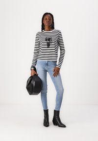 Sorte og hvite stripete langermede skjorte med grafisk trykk, kombinert med lyseblå smale jeans og svarte ankelstøvler. Holder en svart veske.