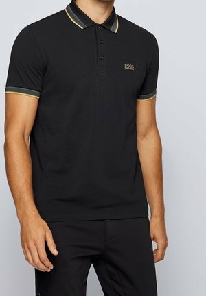 Polo noir avec un col contrastant présentant des rayures vertes et jaunes, manches courtes, et un petit logo brodé sur la poitrine.