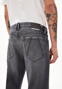 Schwarze Denim-Jeans mit einem verblassten grauen Finish, ausgestattet mit einem markierten Lederpatch, zwei Gesäßtaschen und sichtbaren Ziernähten.