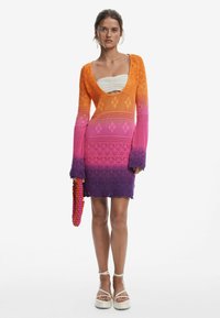 Abito a maglia con una sfumatura ombré che va dall'arancione al viola. Presenta maniche lunghe, un profondo scollo e orlo a zig zag. Decorato con una borsa di perline.