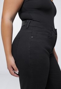 Zwarte denim jeans met een hoge taille, met een gladde textuur, vijf zakken en een leren patch op de achterkant van de tailleband.