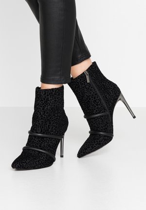 Bottines à imprimé léopard noir en tissu texturé avec des talons stilettos prononcés et des brides accentuantes autour du métatarse.