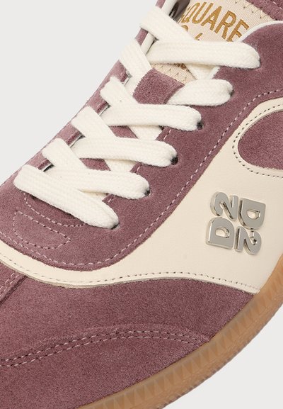Gros plan d'une basket en daim mauve et crème avec des lacets blancs, un logo en métal "2ND" et une semelle en gomme marron.