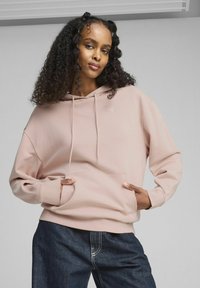 Sudadera con capucha de un rosa claro, que cuenta con un bolsillo frontal, cordones y puños acanalados. Combinada con jeans de mezclilla oscura y un pequeño detalle de logo.