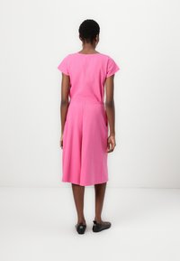 Ροζ ζιπ-κιλότ κοντομάνικο φτιαγμένο από βαμβάκι, με ελαστική μέση και φαρδιά, ρέουσα ποδιά, παρουσιασμένο από πίσω.