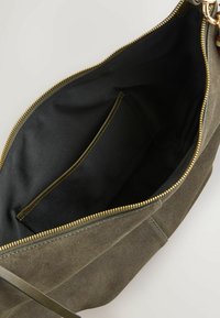 Sac bandoulière en daim vert olive avec fermeture éclair dorée, intérieur en tissu noir et poche intérieure plate.