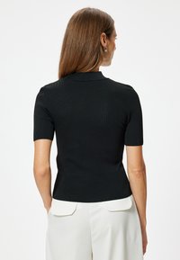 Top negro de manga corta con diseño acanalado y cuello tipo polo, que presenta un corte ajustado. Combinado con pantalones blancos de tiro alto con bolsillos traseros.