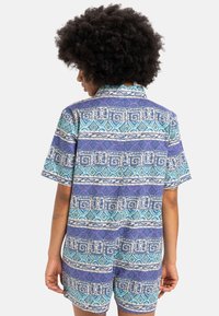 Short-sleeve, collared romper in blue and purple geometric patterns, featuring a relaxed fit and textured fabric.