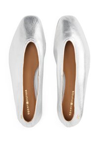 Ballerines argentées avec une finition métallique brillante, design à bout carré, côtés découpés et semelles intérieures beige. Accent logo doré sur le côté.