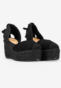 Black wedge espadrilles with a suede upper, woven jute sole, and a textured black fabric slingback with bow detail.