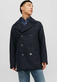 Giacca peacoat della marina in misto lana, con un design doppiopetto, ampi revers e sei bottoni neri. Indossata sopra una camicia di denim.