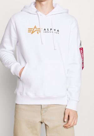 Sudadera blanca hecha de una tela suave, con un bolsillo frontal, cordones y un bolsillo con cremallera en la manga con una etiqueta roja. Logo en negro y dorado.