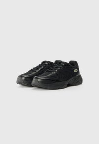 Black athletic shoes with textured mesh and synthetic panels. Features a lace-up design and a small green logo on the side.