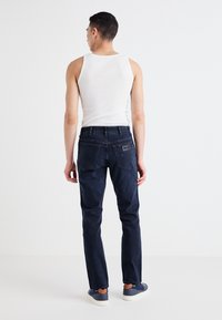 Tumedat sinised denim teksad sirge säärtega, millel on tagataskud ja nahaabel vöökoht. Kombineeritud valge tank-topiga.