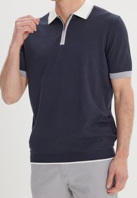Koszulka polo z krótkim rękawem w ciemnym granacie z białym i szarym kołnierzykiem, zamkiem błyskawicznym i teksturowanymi mankietami. Miękka dzianina, klasyczny krój.