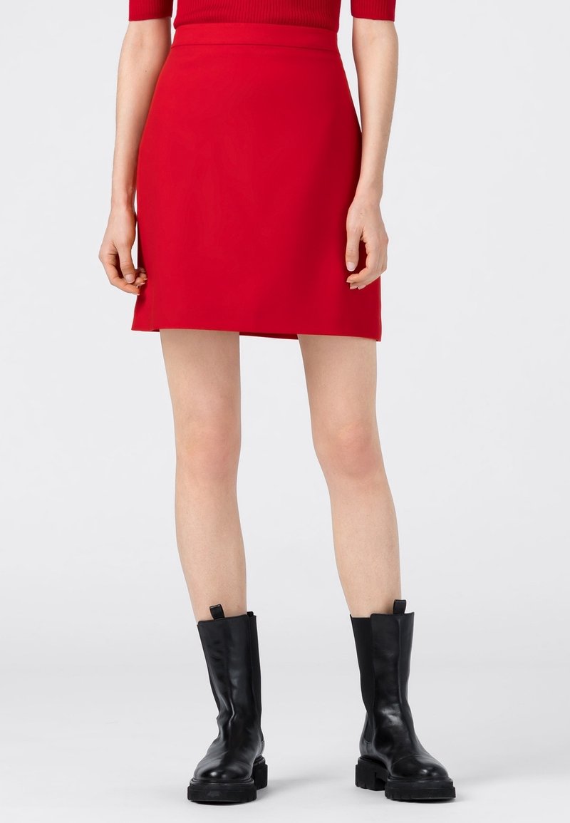 Minifalda roja con una cintura ajustada, textura suave y sin cierres visibles, combinada con botas negras hasta el tobillo con una suela gruesa.