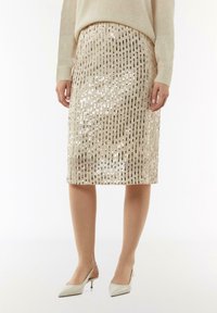 Beige Pailletten-Bleistiftrock mit vertikalen Streifen; knielang. Getragen mit einem hellen Pullover und spitz zulaufenden Absätzen.