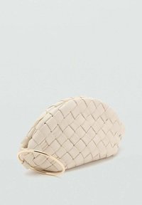 Borsa clutch intrecciata beige con una forma curva, dotata di una maniglia circolare dorata, posizionata su uno sfondo grigio chiaro.