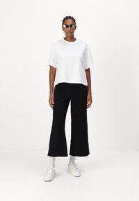 Fehér pamut crop póló rövid ujjakkal, fekete, széles lábú nadrággal, oldalsó csíkkal kombinálva. A szettet fehér sportcipő egészíti ki.