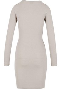 Langermet knelengdedrakt i lys beige stoff med en subtil glitring. Har rund hals og tettsittende silhuett. Glatt tekstur.