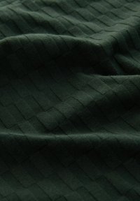 Tamnozeleno pleteni materijal s uzdignutim uzorkom mreže koji stvara teksturiranu, mekanu i blago naboranu površinu.
