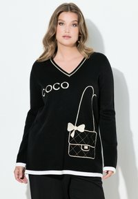 Suéter negro de punto con escote en V y ribete blanco, que presenta la palabra "COCO" y un diseño bordado de un bolso con un lazo.