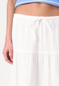 Falda blanca texturizada con cintura ajustable. Presenta un corte relajado y un diseño gather que añade volumen. Vista de cerca de la cintura.