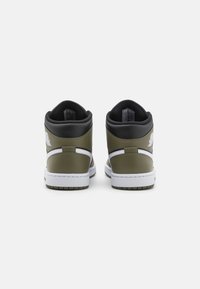 High-top sneakers in olive green and black leather, featuring white accents, smooth texture, and a rubber outsole with a patterned tread.