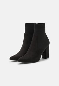 Stivali neri alla caviglia con punta affusolata, realizzati in un materiale simile alla suede, con una parte superiore in maglia a coste e un tacco a blocco.