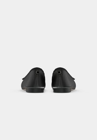 Mustat liukupohjaiset kengät, joissa on sileä pinta, pyöreä kärki, minimalistinen muotoilu ja hienovarainen metalliyksityiskohta korossa.