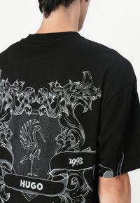 Black cotton t-shirt featuring white graphic print of a bird, decorative swirls, and date 1993, with a classic crew neck design.
