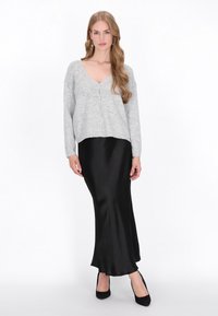 Cardigan gri tricotat cu decolteu în V și închidere cu nasturi, asortat cu o fustă maxi din satin negru, cu o textură netedă. Pantofi cu toc înalt negri.
