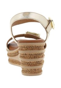 Sandales compensées dorées à lanières avec un talon en jute tressé, un dessus texturé et une fermeture à boucle réglable. La semelle intérieure beige doux complète le design.