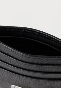 Εσωτερικό μαύρου δερμάτινου πορτοφολιού με πολλαπλές θήκες για κάρτες. Υφή φινιρίσματος και ραμμένα άκρα, παρουσιάζοντας ένα ομαλό, κομψό σχέδιο.