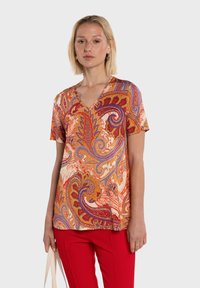 Haut à manches courtes et col en V avec un motif cachemire vibrant aux teintes orange, rouge et violet. Tissu léger avec une coupe décontractée, assorti à un pantalon rouge.