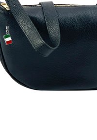 Zwarte leren schoudertas met een gestructureerd oppervlak, gouden rits en een klein Italiaans vlaggetje dat aan de schouderband is bevestigd.