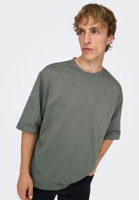 T-shirt à manches courtes vert olive, coupe décontractée, en coton doux, avec un col rond et des détails de couture minimalistes.