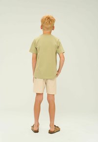 Lichtgroen T-shirt met korte mouwen en een rechte snit, gecombineerd met beige linnen shorts. Bruine sandalen met strikken maken de outfit compleet.