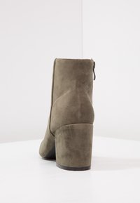 Botines de ante verde oliva con tacón ancho, que cuentan con una cremallera lateral y una textura suave con detalles de costura mínimos.