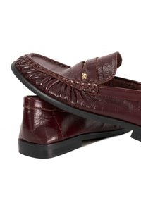 Burgundy leather loafers with a ruched design, contrasting texture details, gold hardware accent, and a rubber sole for traction.